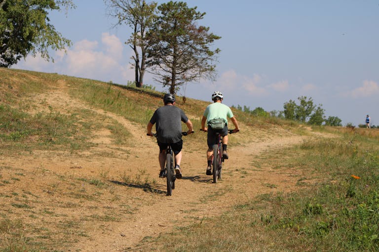 Two men cycling on a sunny dirt trail, enjoying an outdoor adventure and exercise.