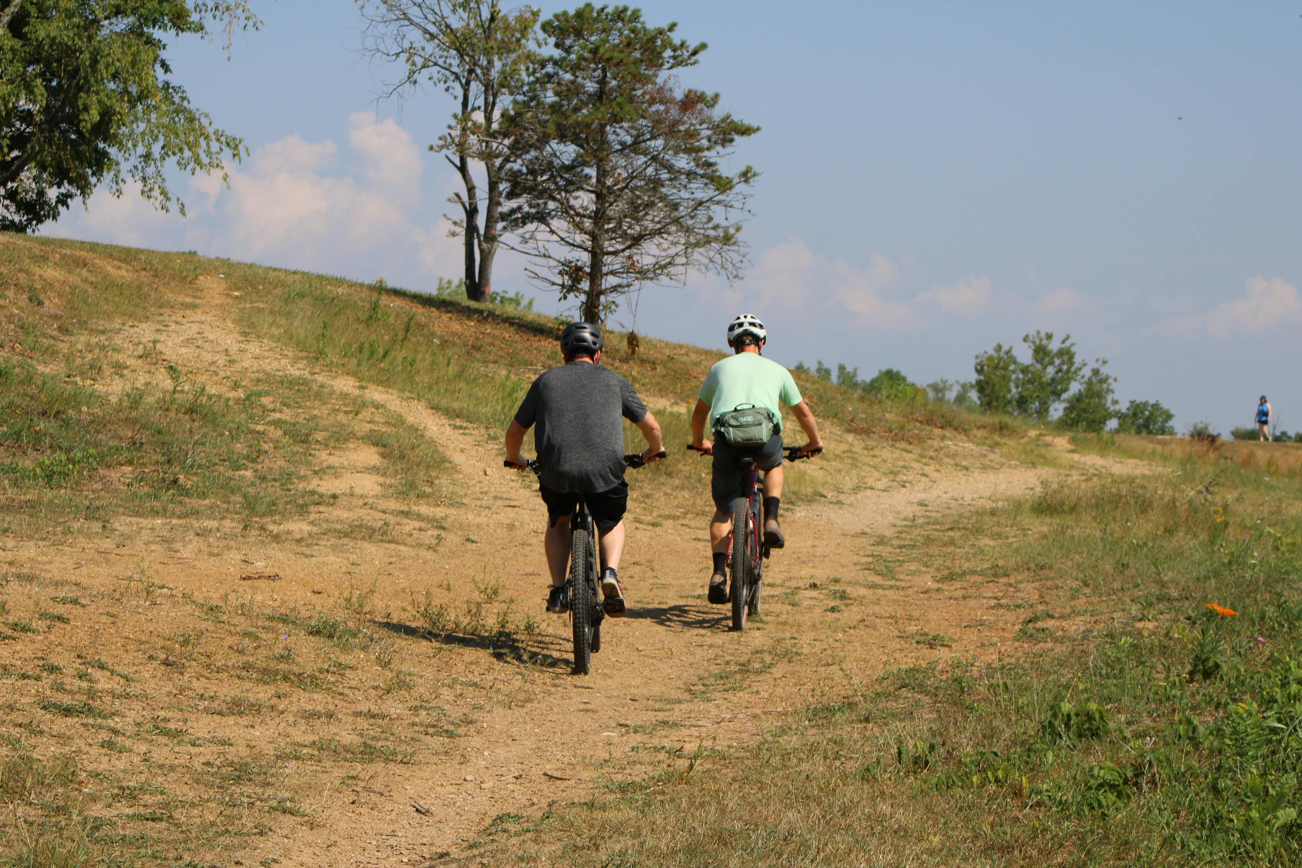 Two men cycling on a sunny dirt trail, enjoying an outdoor adventure and exercise.