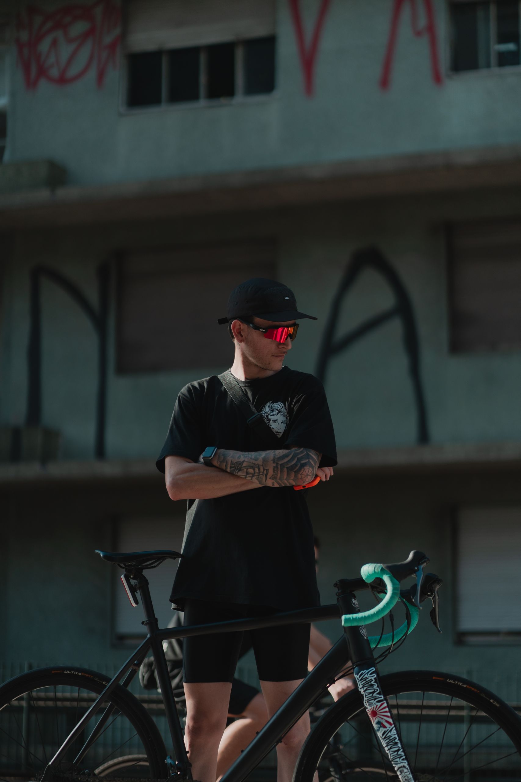 A trendy adult male cyclist poses with his bicycle against an urban backdrop.