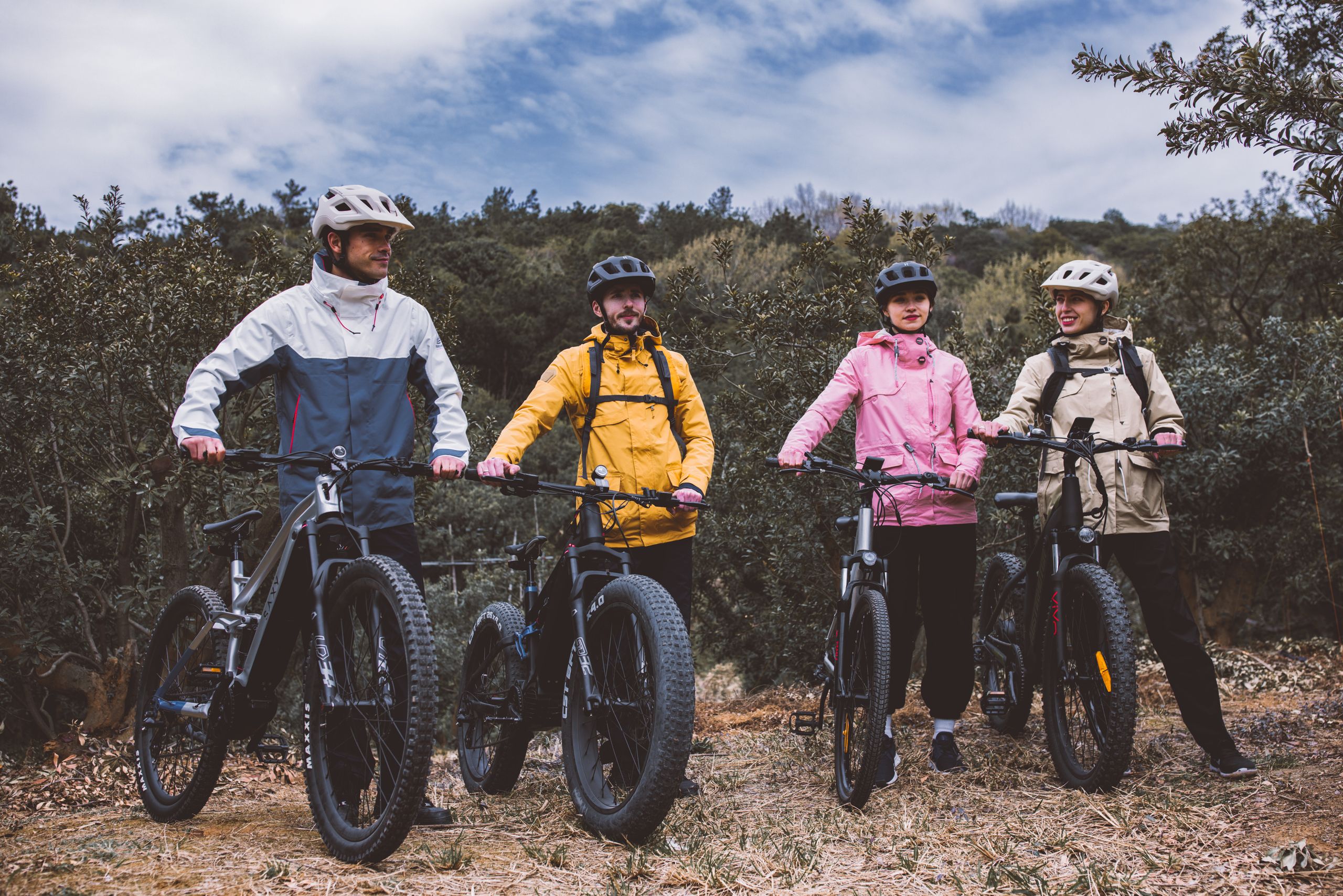 Four adults with mountain bikes pause during an outdoor adventure on an overcast day.