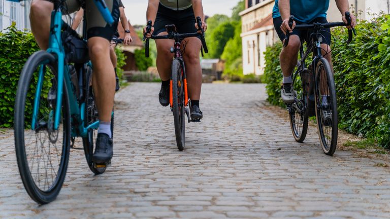Group of cyclists riding on a cobblestone street surrounded by greenery on a sunny day.