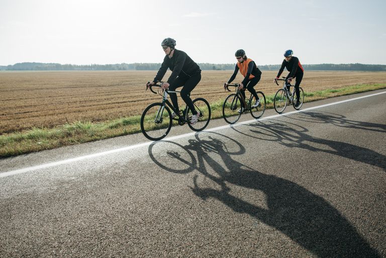 Three cyclists enjoy a leisurely ride on a rural road surrounded by fields