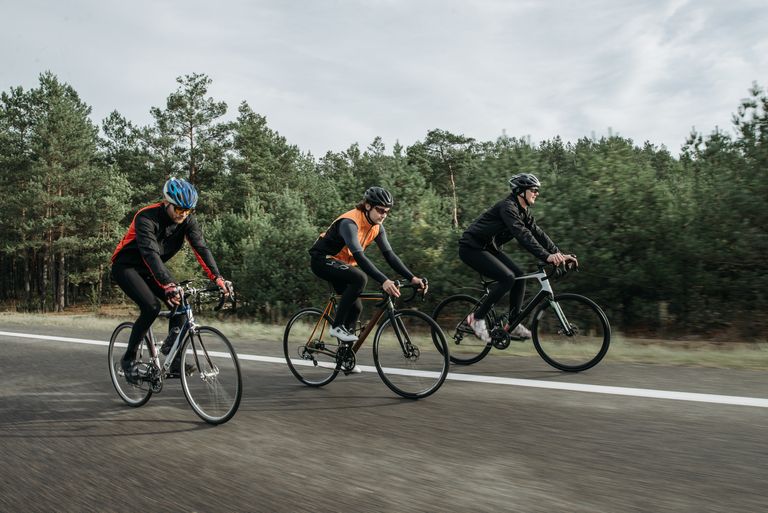 Three cyclists riding on an open road near a forest, showcasing sport and transportation.