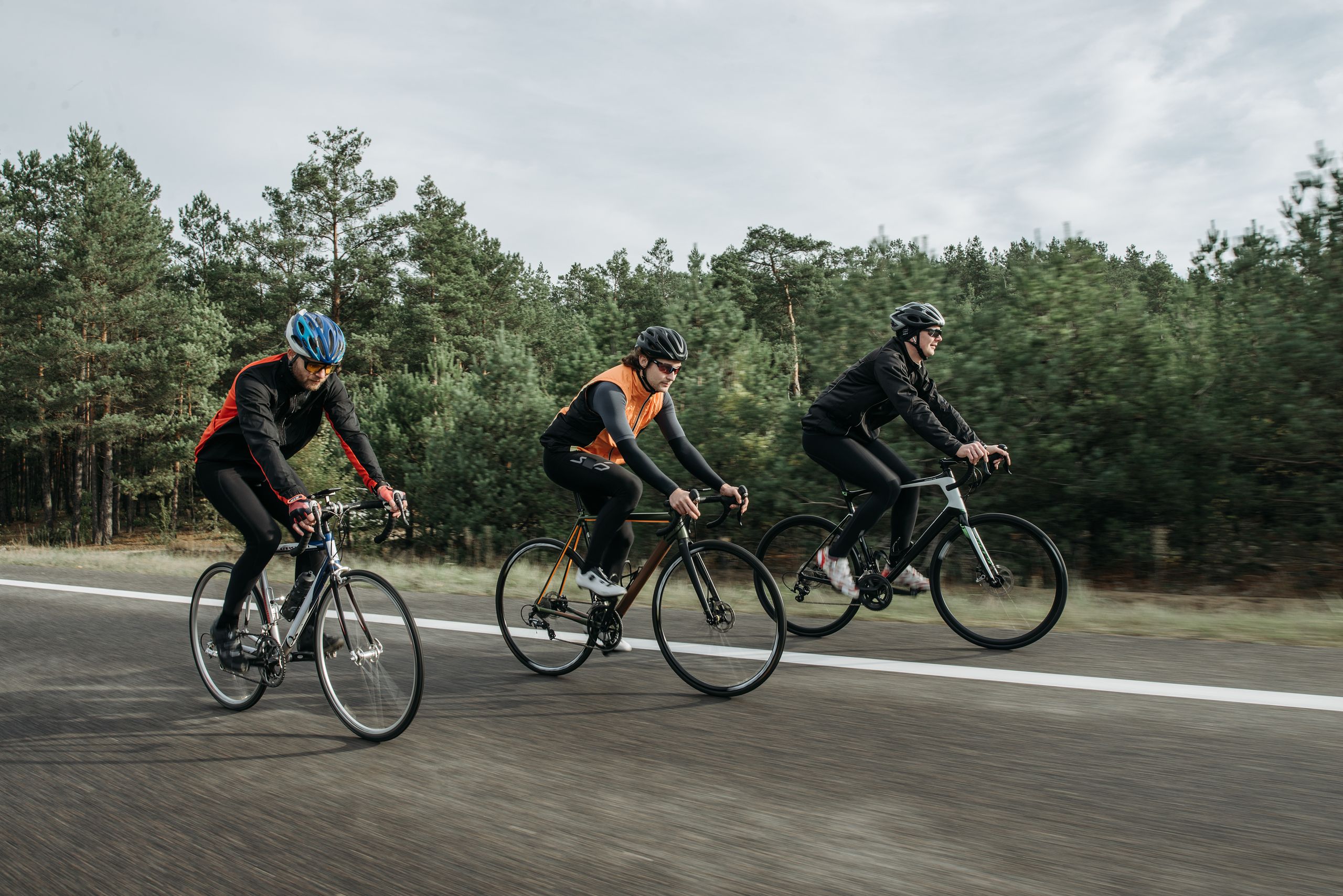 Three cyclists riding on an open road near a forest, showcasing sport and transportation.