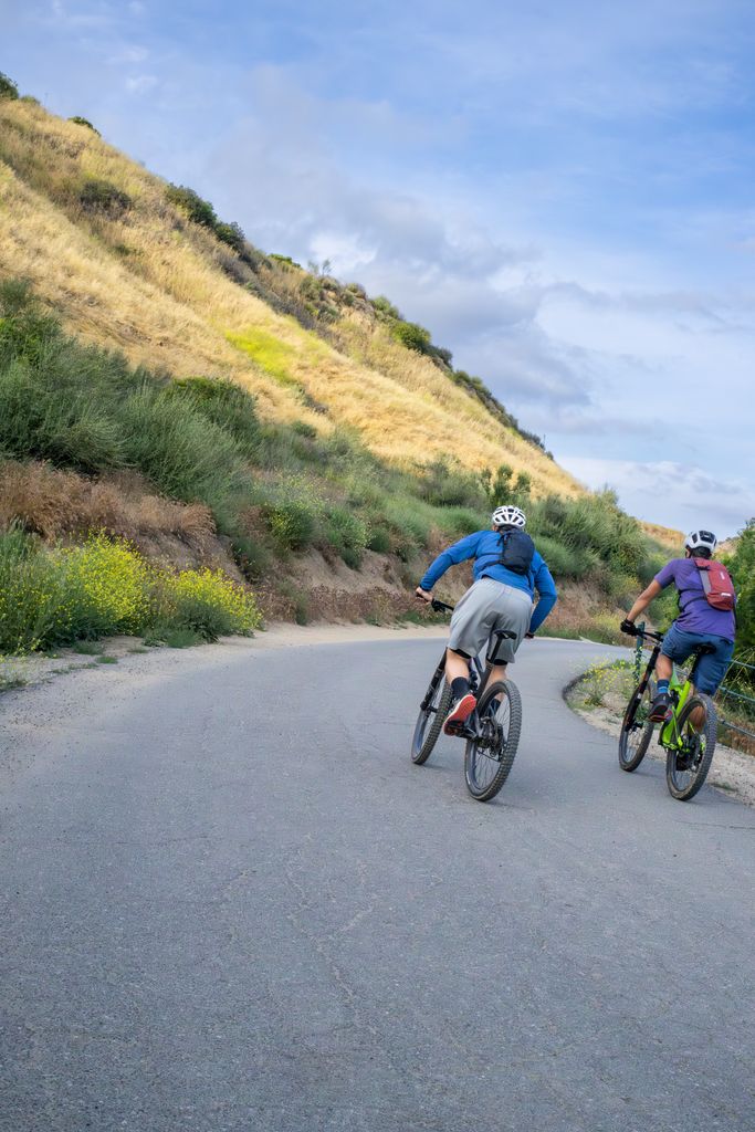 Two cyclists enjoy a scenic ride on a winding rural road wearing helmets and sportswear.