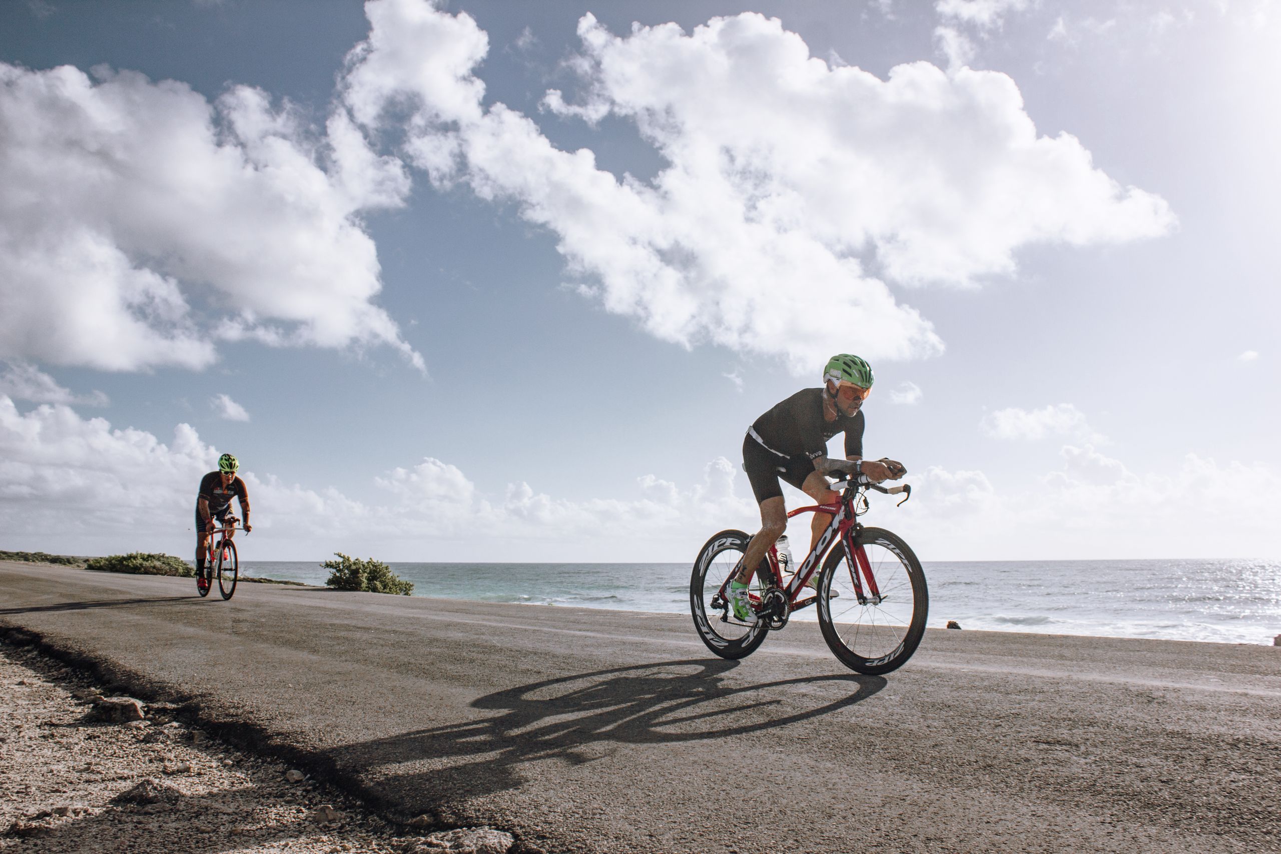Two cyclists enjoying a ride along a scenic coastal road under a bright sky.
