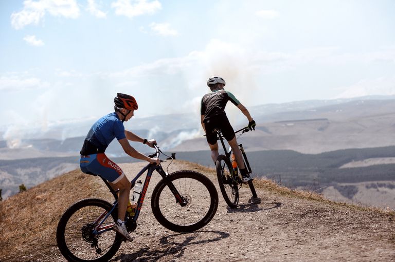 Two mountain bikers enjoy a scenic ride on a hilltop trail under a clear sky.