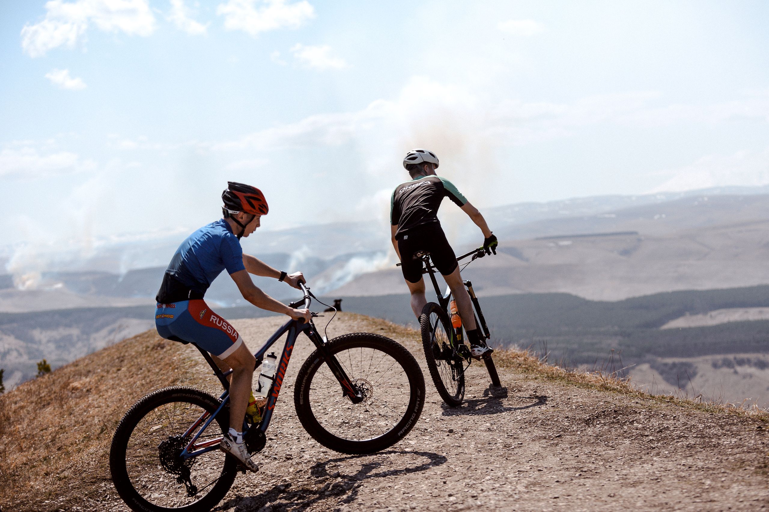Two mountain bikers enjoy a scenic ride on a hilltop trail under a clear sky.