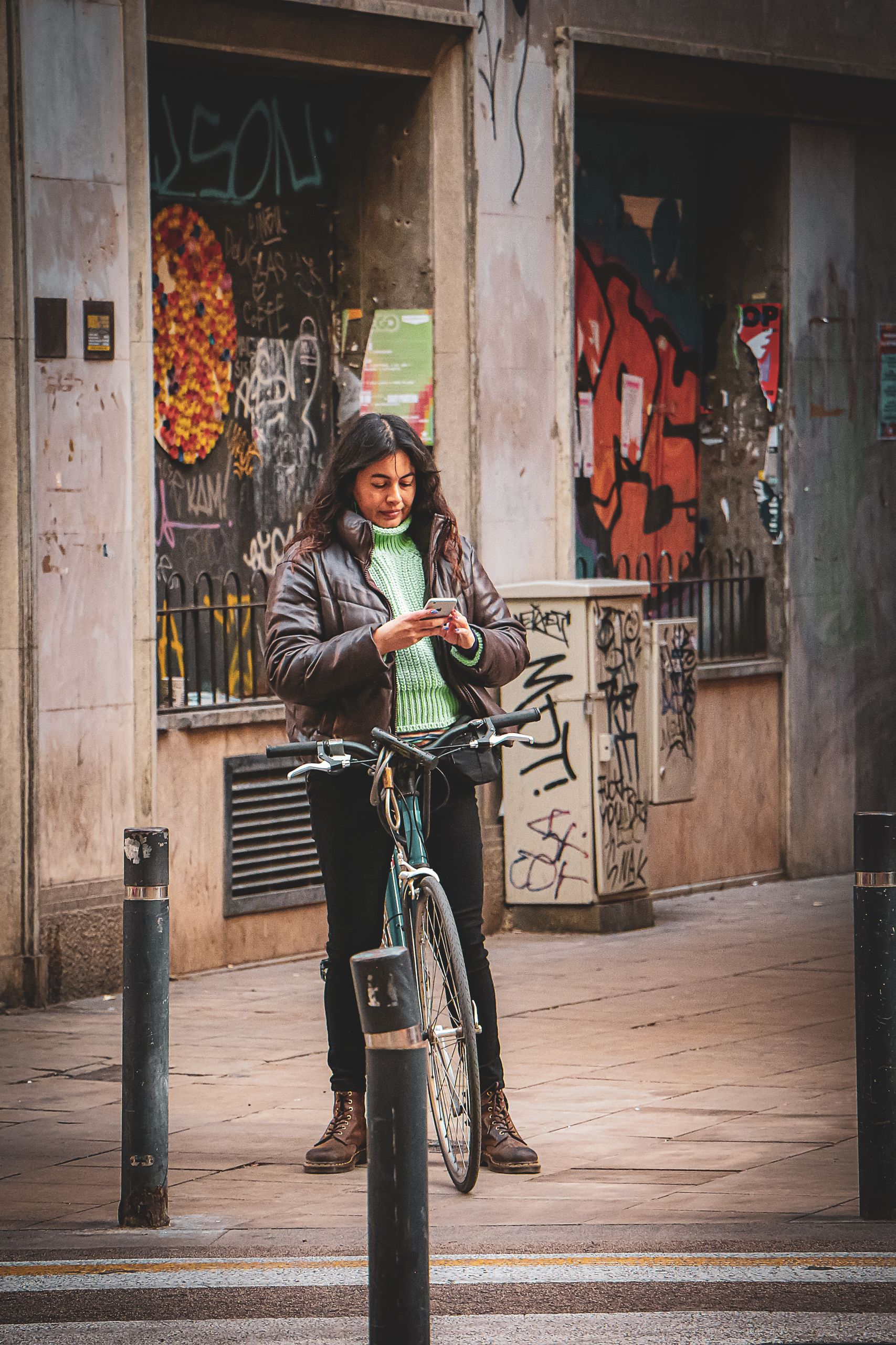 Young woman standing beside her bicycle on a graffiti-decorated street in Barcelona.